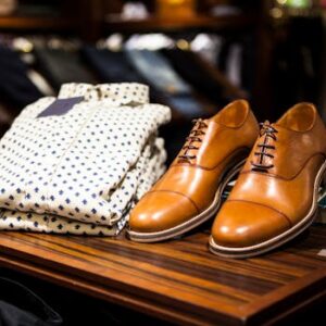 Elegant brown leather shoes and printed shirt displayed on a wooden table in a stylish clothing store.